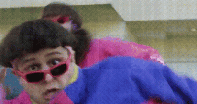 A Woman Wearing Red Sunglasses And A Pink Jacket Is Standing Next To Another Woman Wearing A Blue Jacket . GIF
