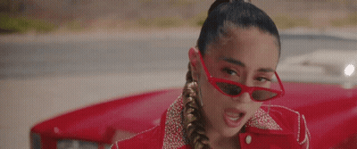 A Woman Wearing Red Sunglasses And A Red Jacket Is Standing Next To A Red Car . GIF