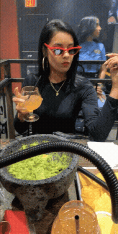 A Woman Wearing Red Sunglasses Sits At A Table With A Bowl Of Guacamole On It GIF