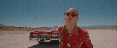A Woman Wearing Red Sunglasses Stands In Front Of A Red Cadillac GIF