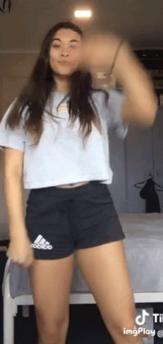 A Woman Wearing Shorts And A Crop Top Is Dancing In A Bedroom . GIF