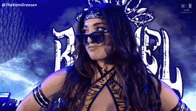 A Woman Wearing Sunglasses And A Bandana Is Standing In Front Of A Wrestling Logo . GIF