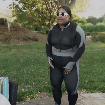 A Woman Wearing Sunglasses And A Black And Grey Jumpsuit GIF