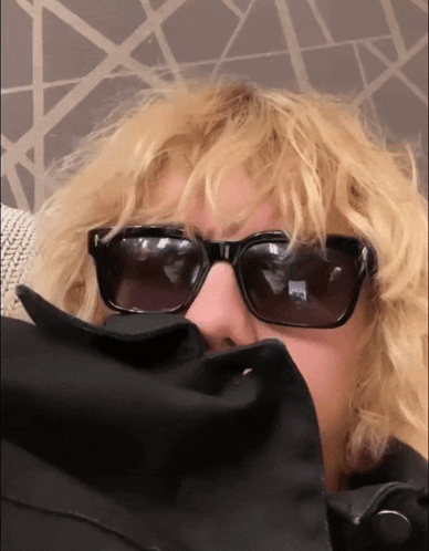 A Woman Wearing Sunglasses And A Black Jacket Covering Her Face GIF