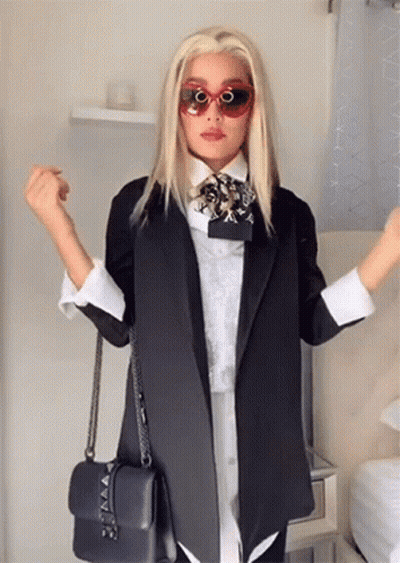 A Woman Wearing Sunglasses And A Black Jacket Holds A Black Purse . GIF
