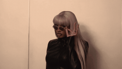 A Woman Wearing Sunglasses And A Black Jacket Making A Peace Sign GIF