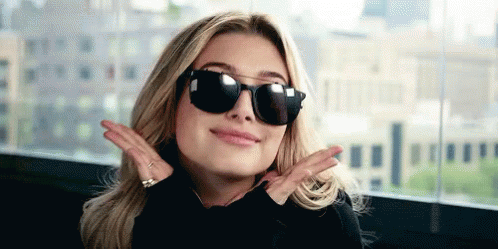 A Woman Wearing Sunglasses And A Black Shirt Is Making A Peace Sign With Her Hands . GIF