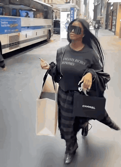 A Woman Wearing Sunglasses And A Chanel Bag Walks Down A Street GIF