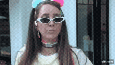 A Woman Wearing Sunglasses And A Colorful Headband Is Standing In Front Of A Building . GIF