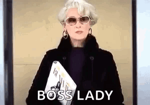 A Woman Wearing Sunglasses And A Fur Coat Is Holding A Magazine And Says Boss Lady . GIF