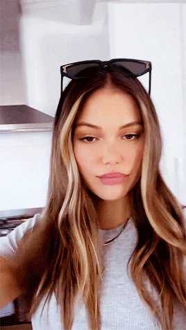 A Woman Wearing Sunglasses And A Gray Shirt Is Taking A Selfie . GIF