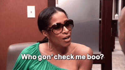 A Woman Wearing Sunglasses And A Green Dress Is Sitting In A Chair And Talking To Another Woman . GIF