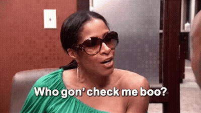 A Woman Wearing Sunglasses And A Green Dress Is Sitting In A Chair And Talking To Another Woman . GIF