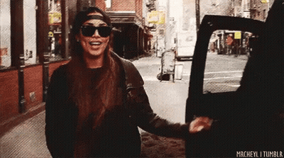 A Woman Wearing Sunglasses And A Hat Is Getting Out Of A Car On A City Street . GIF