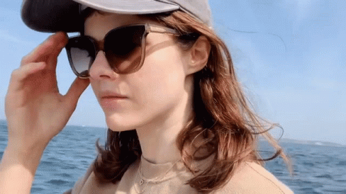 A Woman Wearing Sunglasses And A Hat Looks At The Camera GIF