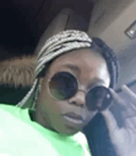 A Woman Wearing Sunglasses And A Head Scarf Is Sitting In A Car . GIF