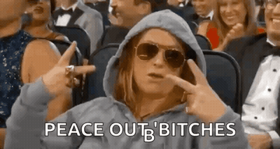 A Woman Wearing Sunglasses And A Hooded Jacket Is Sitting In A Crowd Of People . GIF