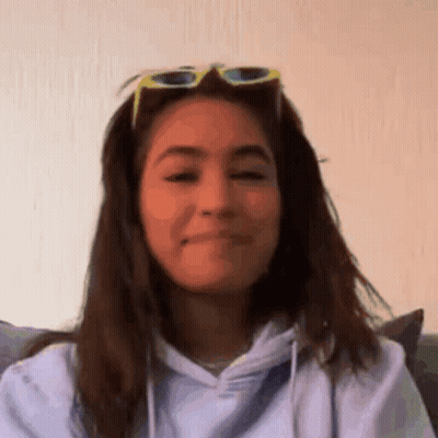 A Woman Wearing Sunglasses And A Hoodie Is Making A Face . GIF