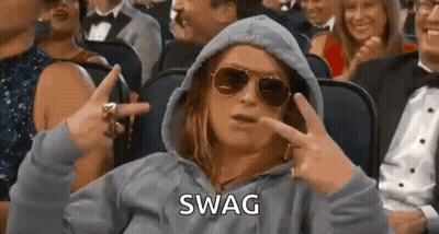 A Woman Wearing Sunglasses And A Hoodie Is Sitting In A Crowd Of People And Making A Swag Sign . GIF