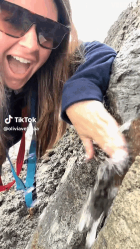 A Woman Wearing Sunglasses And A Lanyard Is Playing With Water On A Rock Wall . GIF