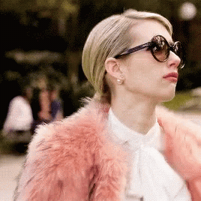 A Woman Wearing Sunglasses And A Pink Fur Coat Looks To The Side GIF