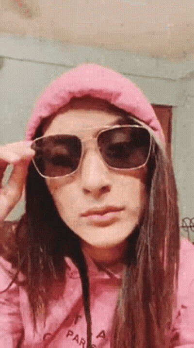 A Woman Wearing Sunglasses And A Pink Hoodie Is Taking Off Her Sunglasses . GIF