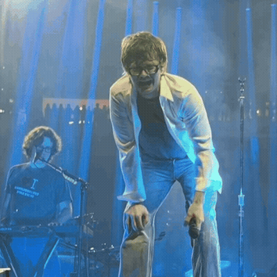 A Woman Wearing Sunglasses And A Pink Jacket Is Kneeling Down On The Sidewalk GIF