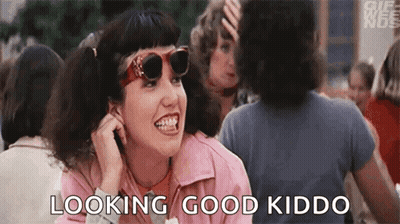 A Woman Wearing Sunglasses And A Pink Jacket Is Sitting In A Crowd Of People And Talking On A Cell Phone . GIF