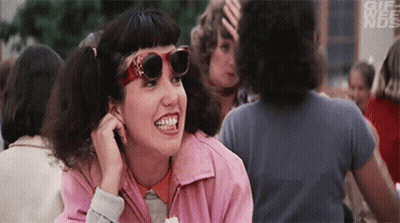 A Woman Wearing Sunglasses And A Pink Jacket Is Smiling In A Crowd . GIF
