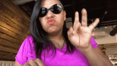 A Woman Wearing Sunglasses And A Pink Shirt Making A Face GIF