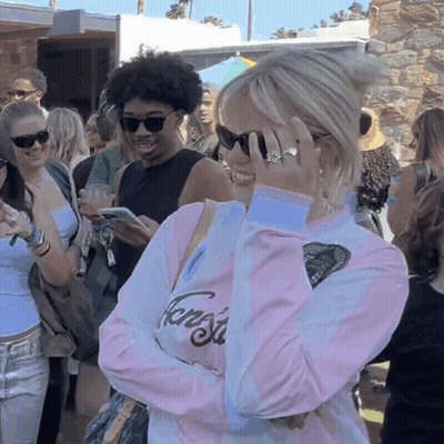 A Woman Wearing Sunglasses And A Pink Shirt That Says Fang Sits In A Crowd GIF