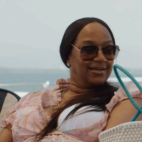 A Woman Wearing Sunglasses And A Pink Top Smiles GIF