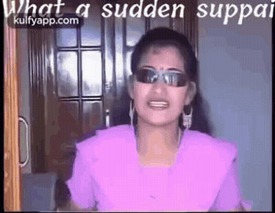 A Woman Wearing Sunglasses And A Purple Shirt Is Standing In Front Of A Door And Talking . GIF