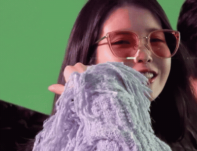 A Woman Wearing Sunglasses And A Purple Sweater On A Green Background GIF