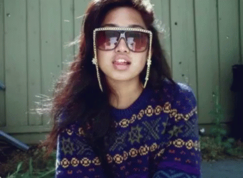 A Woman Wearing Sunglasses And A Purple Sweater With Stars On It GIF
