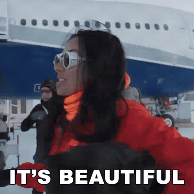 A Woman Wearing Sunglasses And A Red Jacket Says It 'S Beautiful In Front Of A Plane GIF