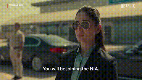A Woman Wearing Sunglasses And A Suit Is Talking To A Man In A Car . GIF