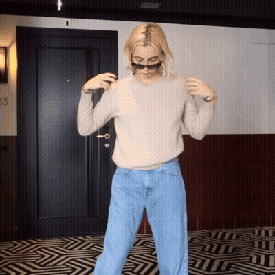 A Woman Wearing Sunglasses And A Sweater Is Standing In Front Of A Door That Has The Number 23 On It GIF