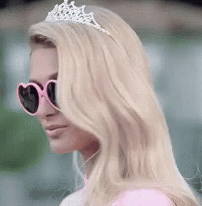 A Woman Wearing Sunglasses And A Tiara Is Standing In Front Of A Green Background . GIF