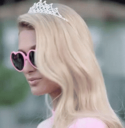 A Woman Wearing Sunglasses And A Tiara Is Wearing A Pink Dress And A Pink Top . GIF