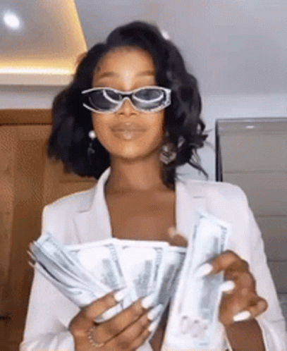 A Woman Wearing Sunglasses And A White Jacket Is Holding A Bunch Of Money . GIF