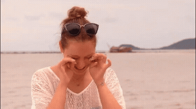 A Woman Wearing Sunglasses And A White Lace Shirt Looks Down GIF