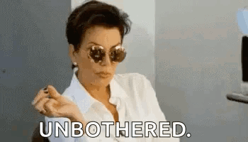 A Woman Wearing Sunglasses And A White Shirt Is Sitting In A Chair And Smoking A Cigarette . GIF