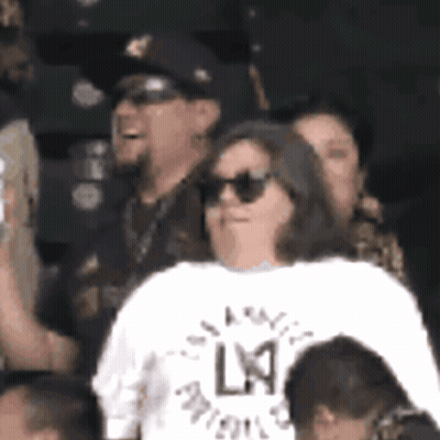 A Woman Wearing Sunglasses And A White Shirt With The Letter L On The Back GIF