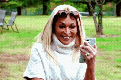 A Woman Wearing Sunglasses And A White Sweater Is Looking At Her Phone GIF