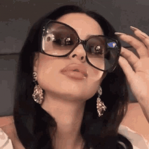 A Woman Wearing Sunglasses And Earrings Is Adjusting Her Glasses . GIF