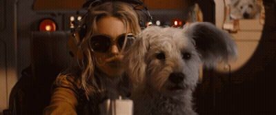 A Woman Wearing Sunglasses And Headphones Holds A Small White Dog GIF