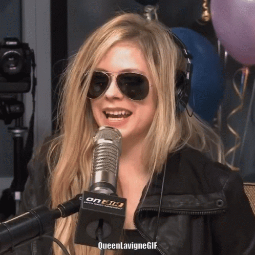 A Woman Wearing Sunglasses And Headphones Is Smiling In Front Of A Microphone That Says On Air On It GIF