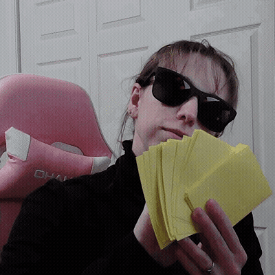 A Woman Wearing Sunglasses And Holding A Stack Of Yellow Cards GIF