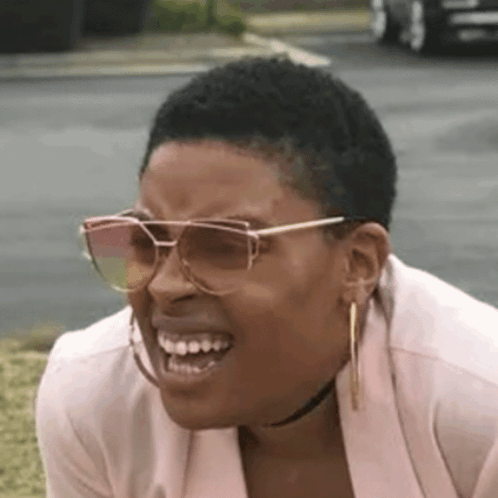 A Woman Wearing Sunglasses And Hoop Earrings Is Making A Funny Face And Smiling . GIF